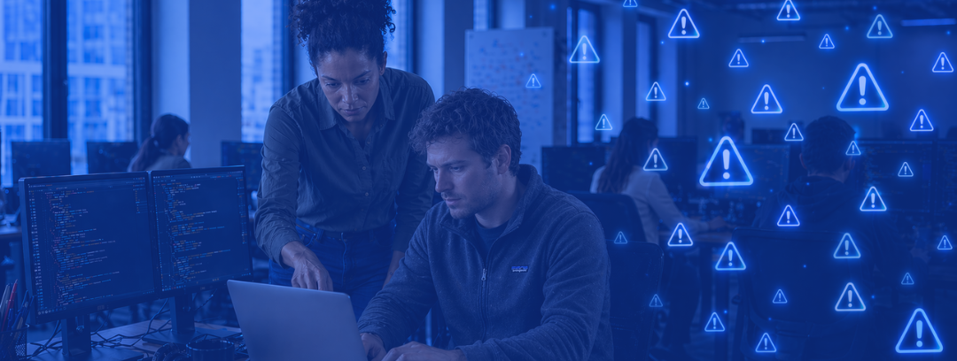 Modern open-plan office scene with a male engineer working on a laptop while a female colleague points at the screen. Two code-filled monitors face him, with several blue alert icons overlaid on the right side.